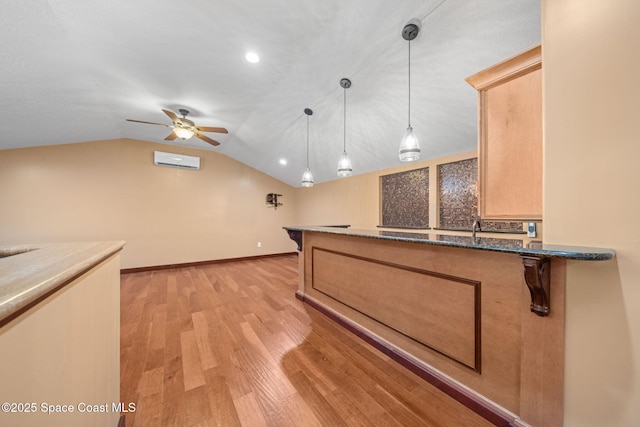 kitchen with an AC wall unit, light brown cabinetry, decorative light fixtures, lofted ceiling, and light wood-type flooring