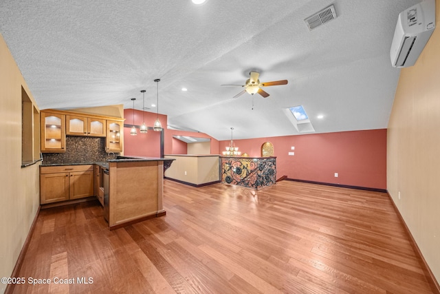 kitchen with lofted ceiling with skylight, pendant lighting, a wall mounted AC, light hardwood / wood-style floors, and a textured ceiling