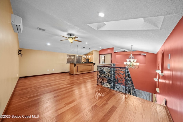 interior space with lofted ceiling, a textured ceiling, light wood-type flooring, an AC wall unit, and ceiling fan with notable chandelier