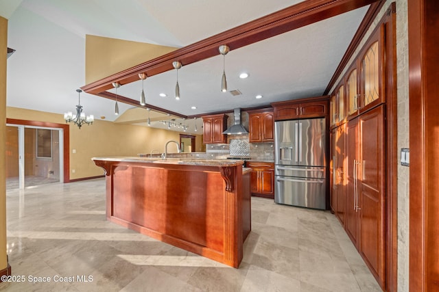 kitchen with pendant lighting, wall chimney range hood, stainless steel refrigerator with ice dispenser, a center island with sink, and decorative backsplash