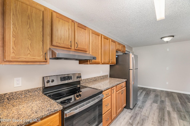 kitchen with appliances with stainless steel finishes, hardwood / wood-style floors, range hood, a textured ceiling, and dark stone counters