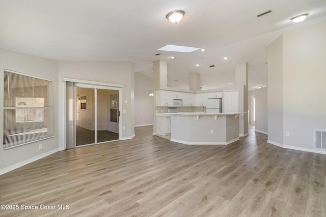 unfurnished living room featuring lofted ceiling with skylight and light wood-type flooring