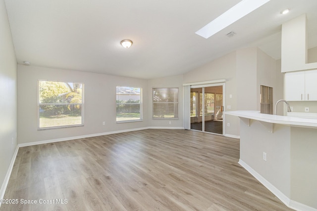 unfurnished living room featuring vaulted ceiling with skylight and light wood-type flooring