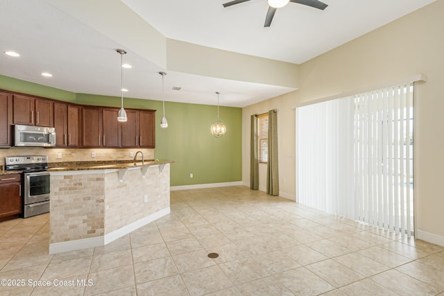 kitchen featuring a breakfast bar, pendant lighting, stainless steel appliances, light stone countertops, and ceiling fan with notable chandelier