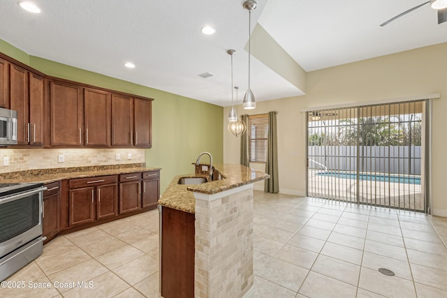 kitchen featuring tasteful backsplash, sink, light stone counters, stainless steel appliances, and a center island with sink