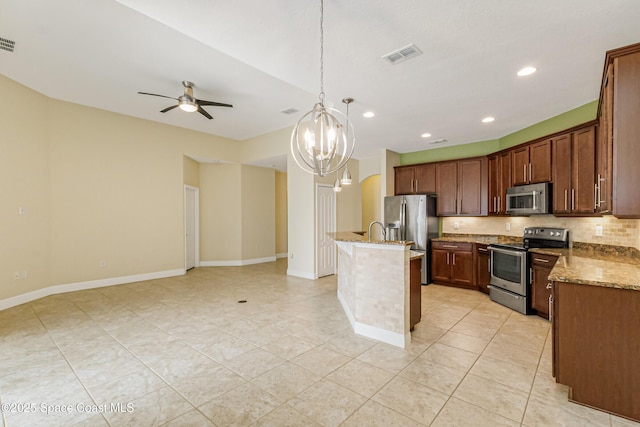 kitchen featuring light stone counters, decorative light fixtures, appliances with stainless steel finishes, a kitchen island with sink, and decorative backsplash