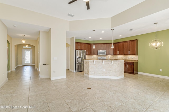 kitchen featuring appliances with stainless steel finishes, decorative light fixtures, ceiling fan with notable chandelier, and a kitchen island