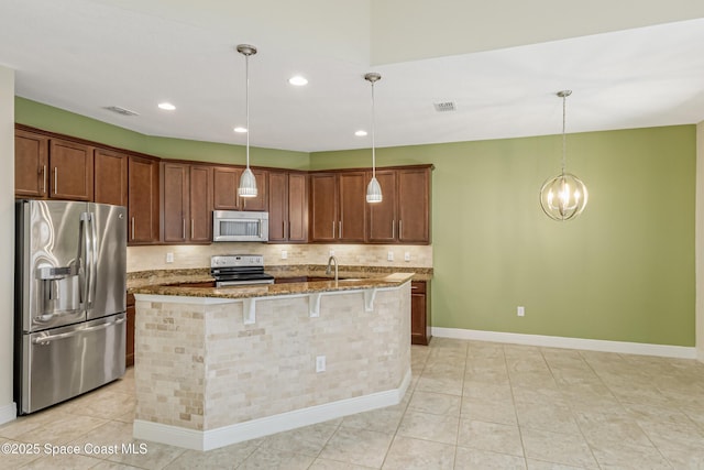 kitchen featuring stainless steel appliances, hanging light fixtures, and a center island with sink