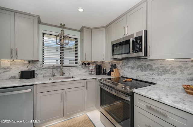 kitchen featuring stainless steel appliances, sink, light stone counters, and decorative backsplash