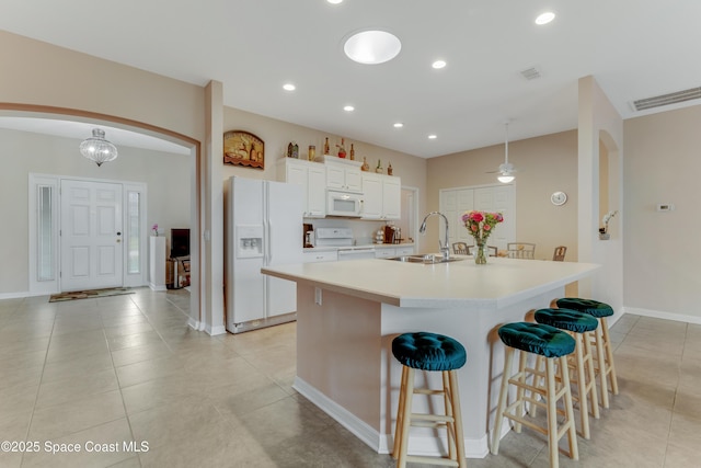 kitchen featuring sink, white appliances, a breakfast bar, white cabinetry, and a large island with sink