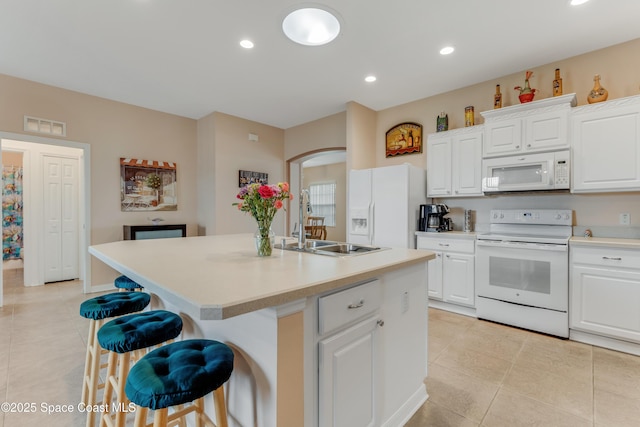 kitchen with sink, white appliances, a breakfast bar area, white cabinetry, and a center island with sink