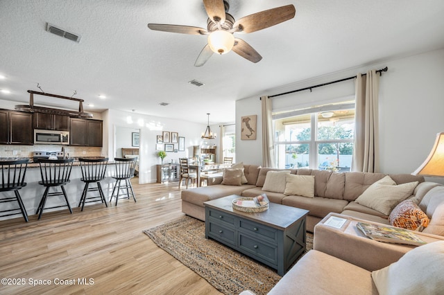 living room featuring a textured ceiling, light hardwood / wood-style flooring, and ceiling fan