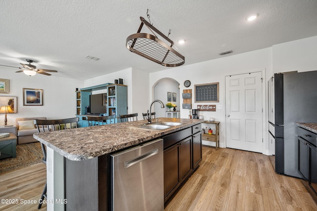 kitchen featuring sink, a textured ceiling, light wood-type flooring, stainless steel appliances, and a kitchen island with sink