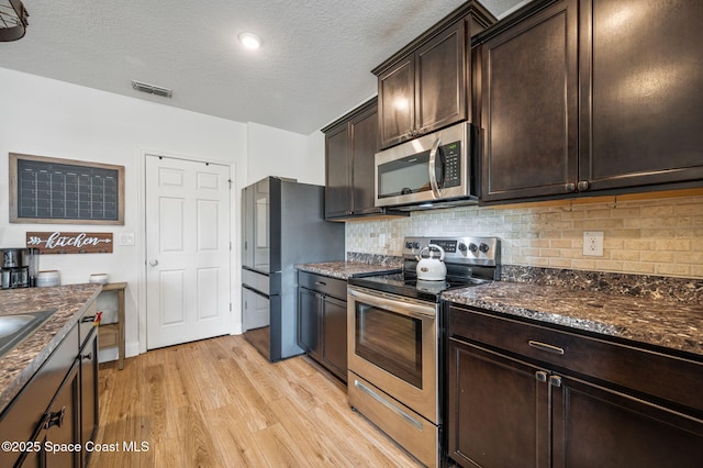 kitchen featuring dark brown cabinetry, a textured ceiling, appliances with stainless steel finishes, light hardwood / wood-style floors, and decorative backsplash