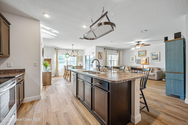 kitchen with dark brown cabinetry, sink, a center island with sink, a kitchen breakfast bar, and stainless steel appliances