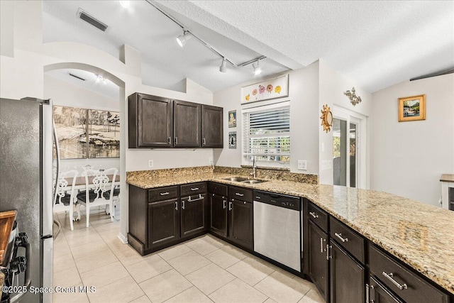 kitchen with vaulted ceiling, appliances with stainless steel finishes, sink, light stone countertops, and dark brown cabinets