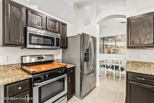 kitchen with appliances with stainless steel finishes, light stone counters, and dark brown cabinetry