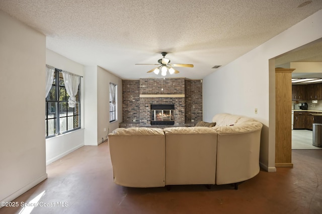 living room featuring ceiling fan, a textured ceiling, and a fireplace