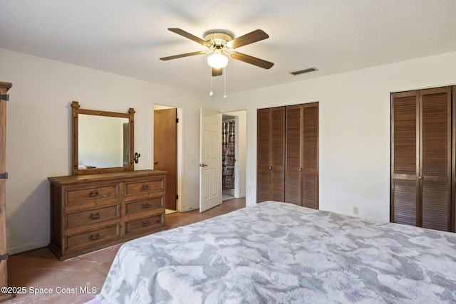 bedroom with ceiling fan, a textured ceiling, and multiple closets