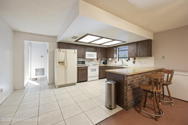 kitchen featuring a kitchen bar, decorative backsplash, light tile patterned floors, kitchen peninsula, and white appliances