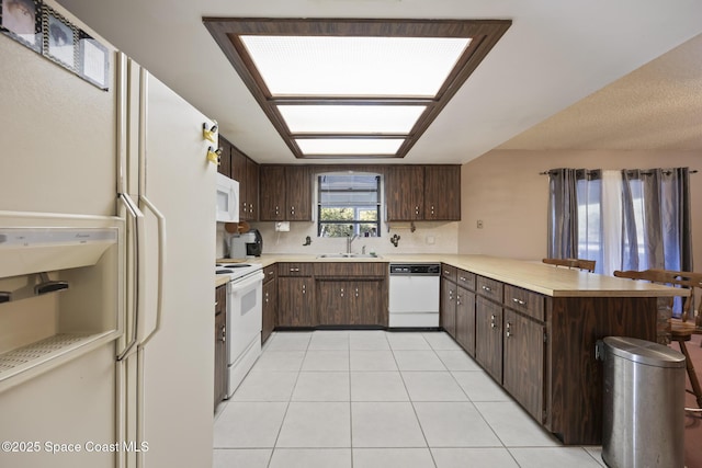 kitchen with sink, light tile patterned floors, kitchen peninsula, dark brown cabinets, and white appliances