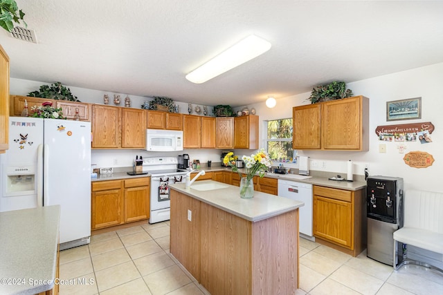 kitchen with sink, white appliances, a center island, a textured ceiling, and light tile patterned flooring