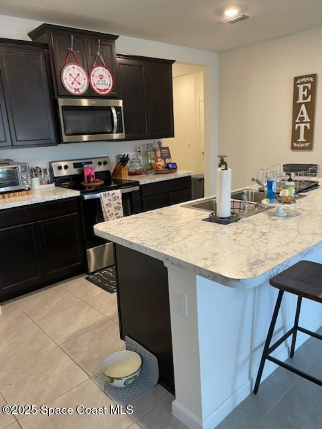 kitchen with light tile patterned flooring, appliances with stainless steel finishes, and a kitchen bar