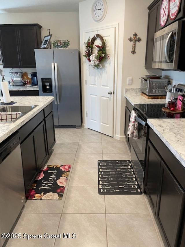 kitchen with light tile patterned flooring, appliances with stainless steel finishes, sink, and light stone counters