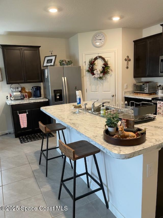 kitchen featuring dark brown cabinetry, a center island with sink, a kitchen breakfast bar, and appliances with stainless steel finishes