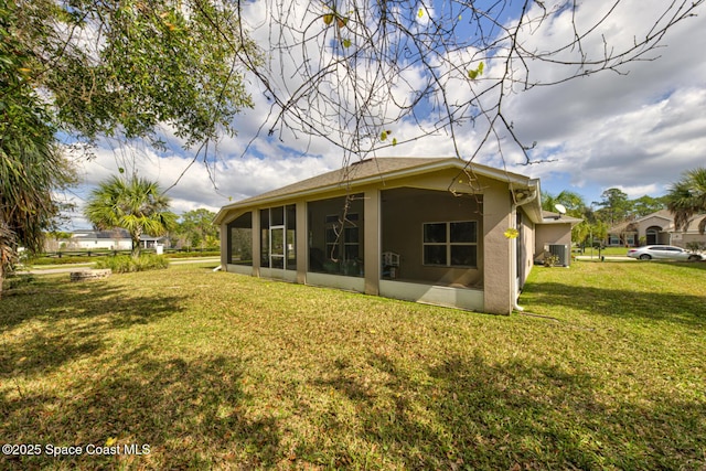 back of property with central AC, a sunroom, and a lawn