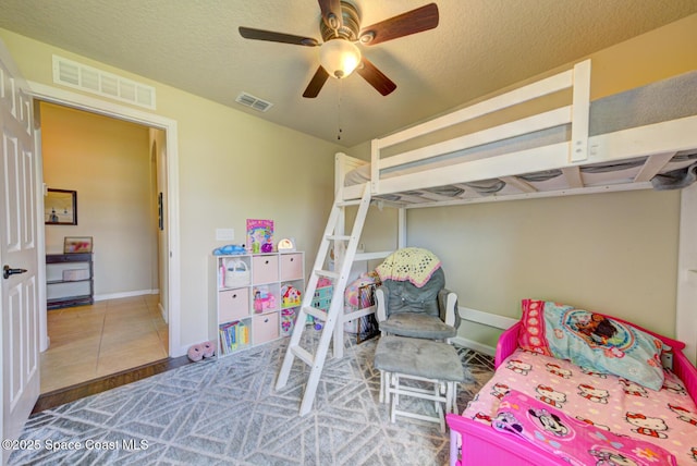 tiled bedroom with ceiling fan and a textured ceiling