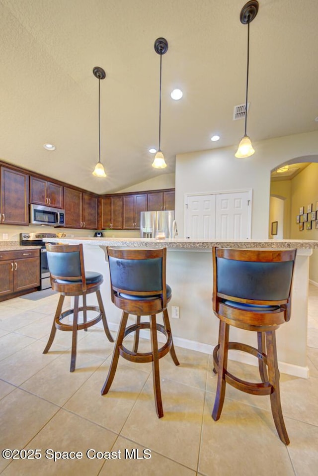 kitchen with light tile patterned flooring, vaulted ceiling, hanging light fixtures, appliances with stainless steel finishes, and a kitchen breakfast bar