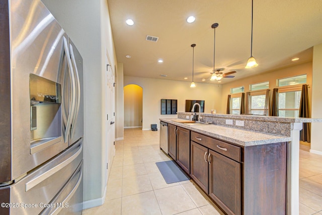 kitchen featuring sink, appliances with stainless steel finishes, hanging light fixtures, light stone countertops, and a center island with sink