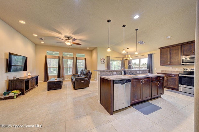 kitchen featuring sink, decorative light fixtures, light tile patterned floors, appliances with stainless steel finishes, and an island with sink