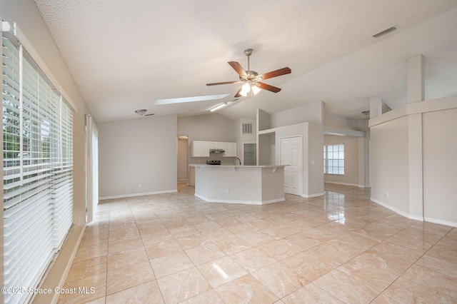 unfurnished living room featuring lofted ceiling, ceiling fan, a textured ceiling, and a healthy amount of sunlight