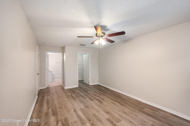 unfurnished bedroom with connected bathroom, a textured ceiling, a walk in closet, a closet, and light wood-type flooring