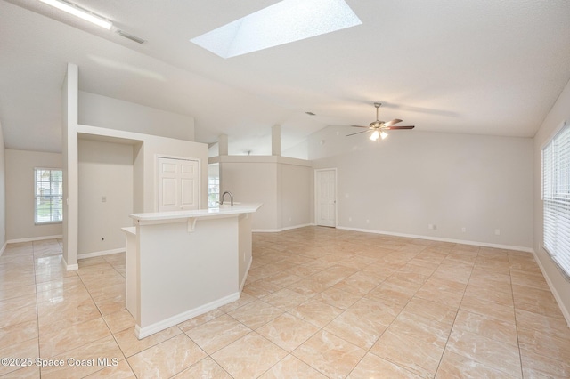 tiled empty room with ceiling fan and vaulted ceiling with skylight