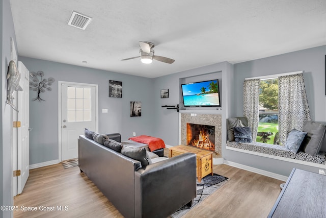 living room with ceiling fan, a premium fireplace, light hardwood / wood-style flooring, and a textured ceiling