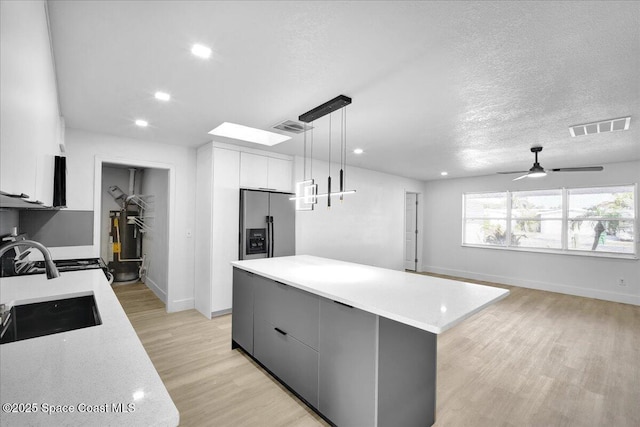 kitchen with sink, stainless steel fridge, hanging light fixtures, a center island, and white cabinets