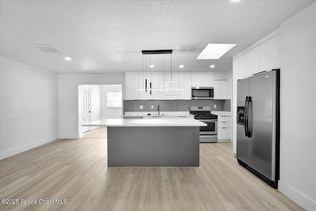 kitchen featuring decorative light fixtures, stainless steel appliances, white cabinets, and a center island with sink