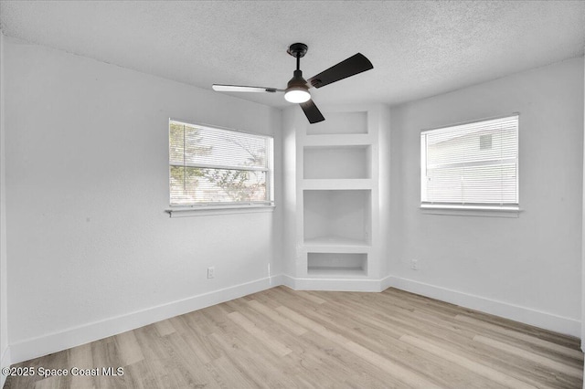 unfurnished room featuring ceiling fan, light wood-type flooring, a textured ceiling, and built in shelves