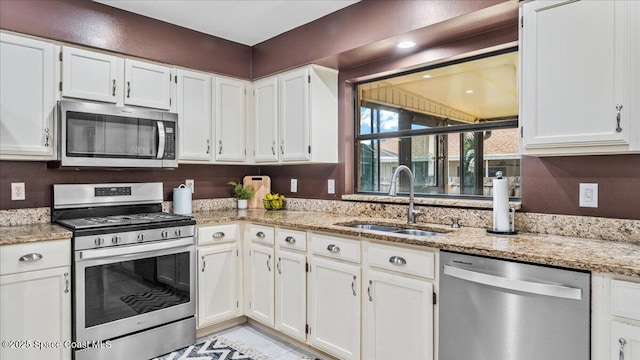 kitchen with stainless steel appliances, white cabinetry, sink, and light stone counters