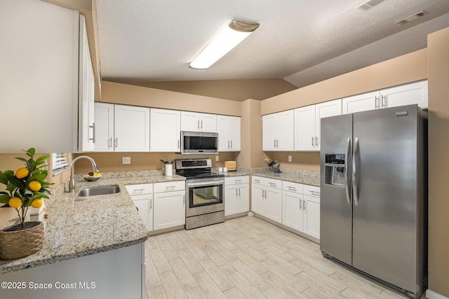 kitchen with stainless steel appliances, white cabinetry, light stone countertops, and sink