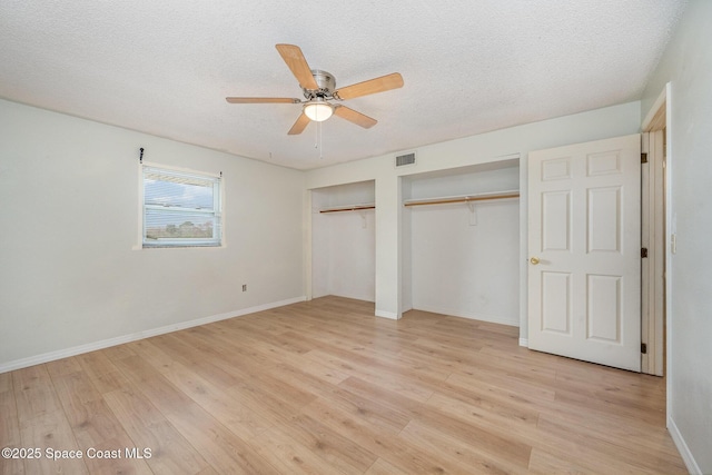 unfurnished bedroom featuring multiple closets, ceiling fan, a textured ceiling, and light hardwood / wood-style flooring