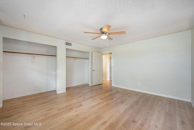 unfurnished bedroom featuring multiple closets, ceiling fan, a textured ceiling, and light wood-type flooring