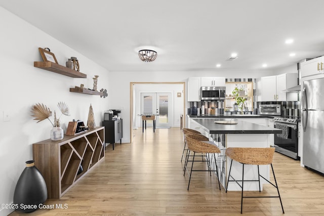 kitchen with appliances with stainless steel finishes, a kitchen breakfast bar, light hardwood / wood-style flooring, and white cabinets