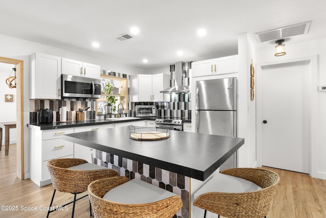 kitchen with appliances with stainless steel finishes, white cabinetry, sink, decorative backsplash, and wall chimney exhaust hood