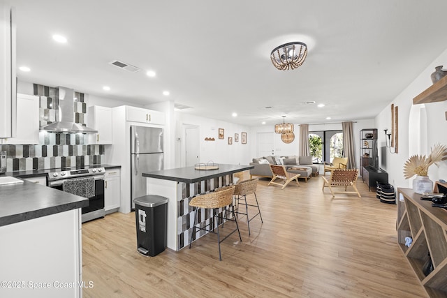 kitchen featuring a breakfast bar area, white cabinetry, stainless steel appliances, a notable chandelier, and wall chimney exhaust hood