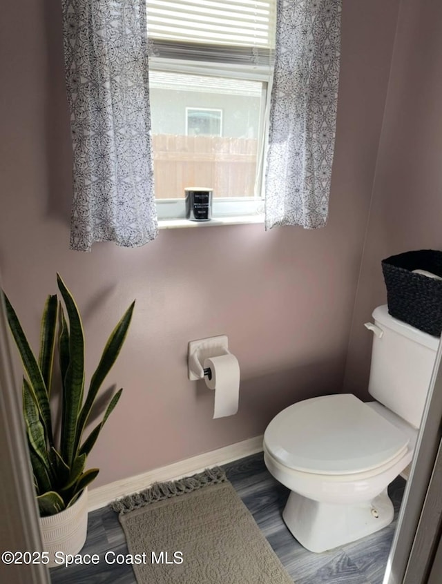 half bath with toilet, baseboards, and wood finished floors