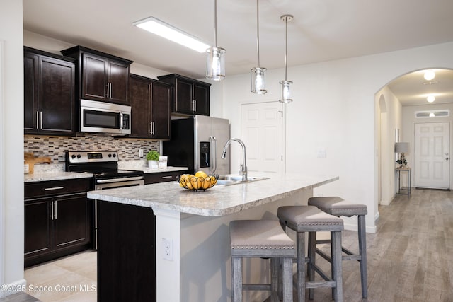 kitchen featuring tasteful backsplash, decorative light fixtures, a kitchen breakfast bar, stainless steel appliances, and a kitchen island with sink